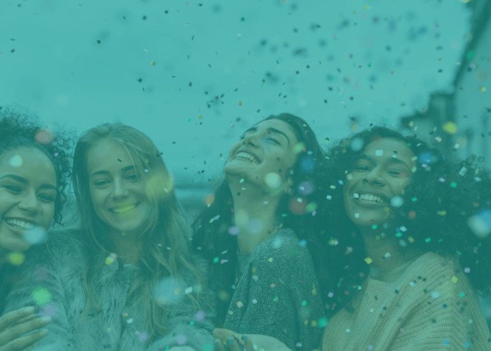 Four women laughing in confetti rain.