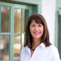 Smiling woman in white shirt near window.