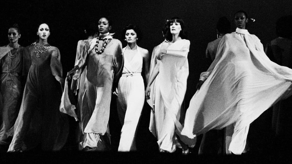 A group of women in white gowns on stage.